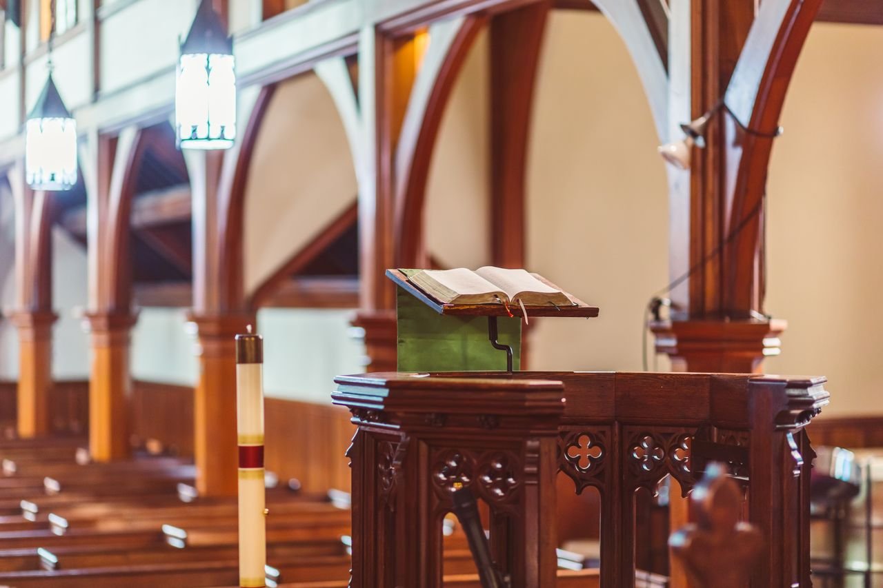 A wooden pulpit with an open Bible in an empty church setting.